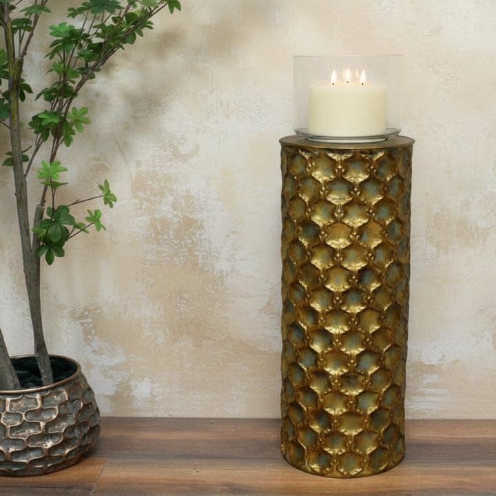 Decorative gold column with a candle next to a potted plant on a wooden floor