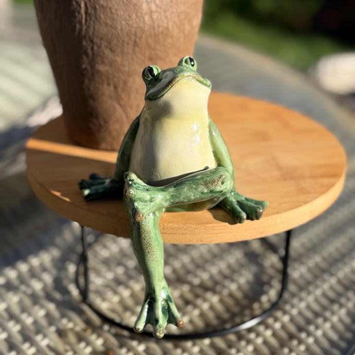 Frog statue on a small round wooden table outdoors
