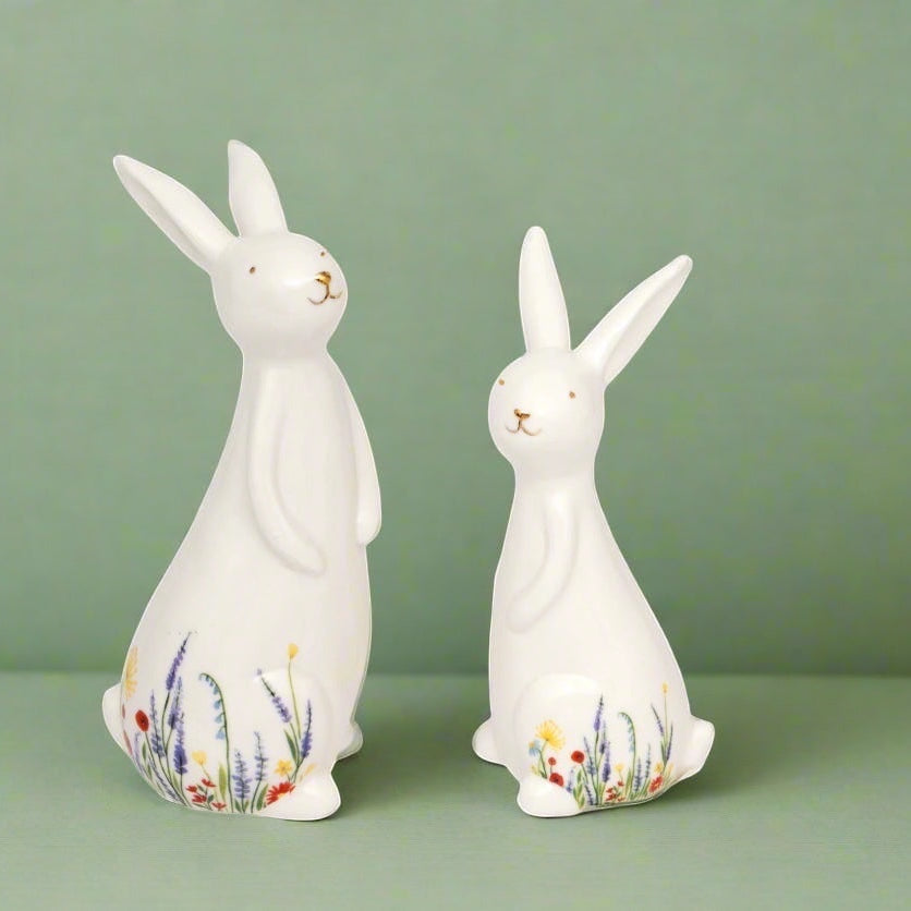 Two white ceramic rabbit figurines with floral designs on a green background
