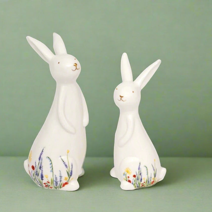 Two white ceramic rabbit figurines with floral designs on a green background
