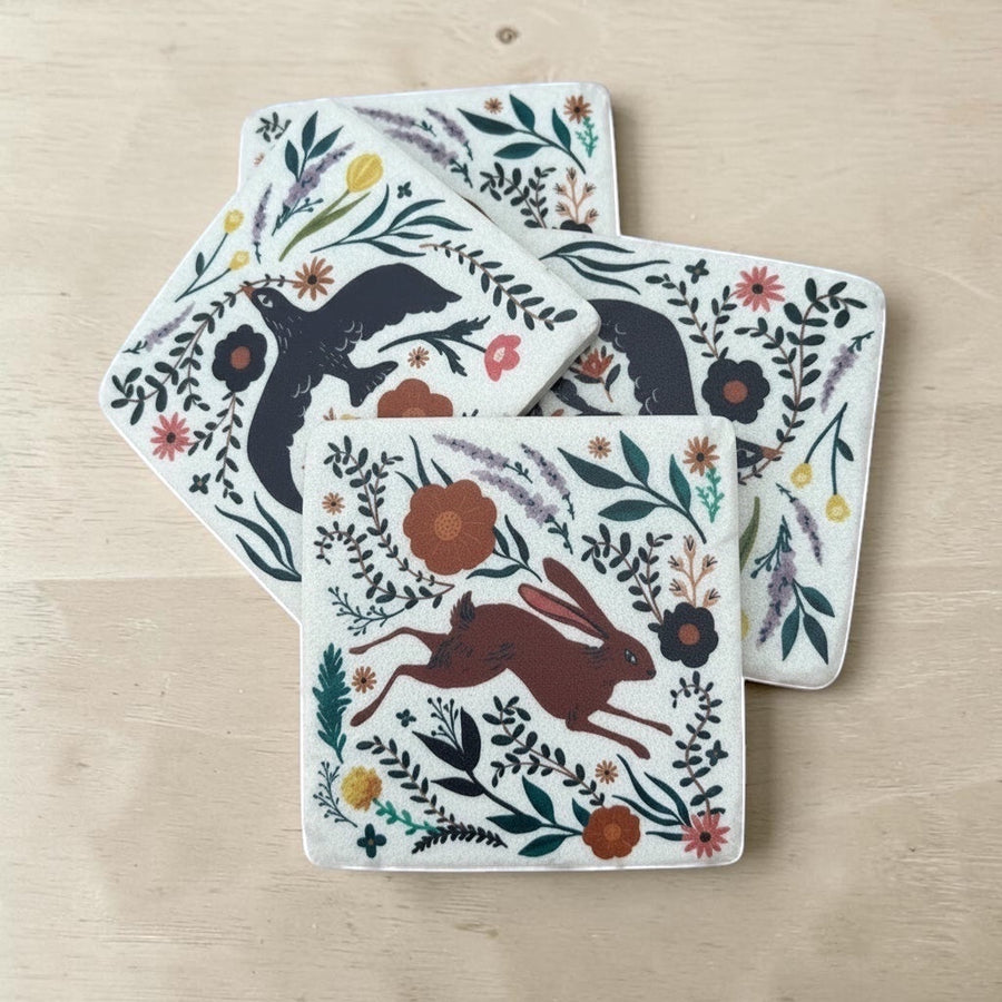 Set of four coasters with animal and floral designs on a wooden surface