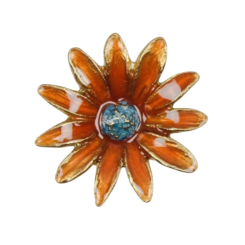 An orange daisy flower brooch with gold-plated metal outlines and a textured blue center, shown on a plain white background.
