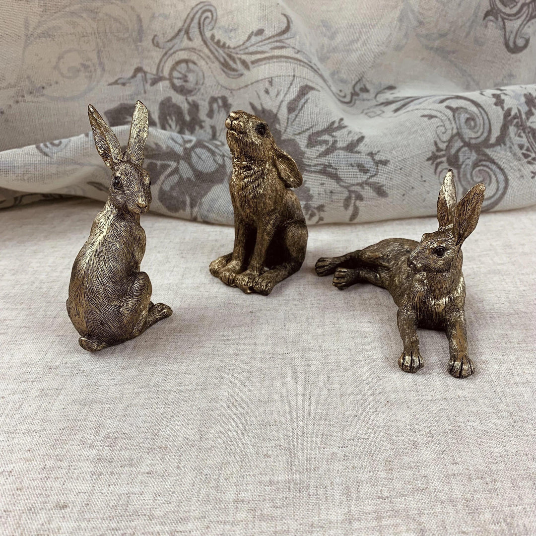 A set of three golden resin hares in different poses placed on a light-colored surface.
