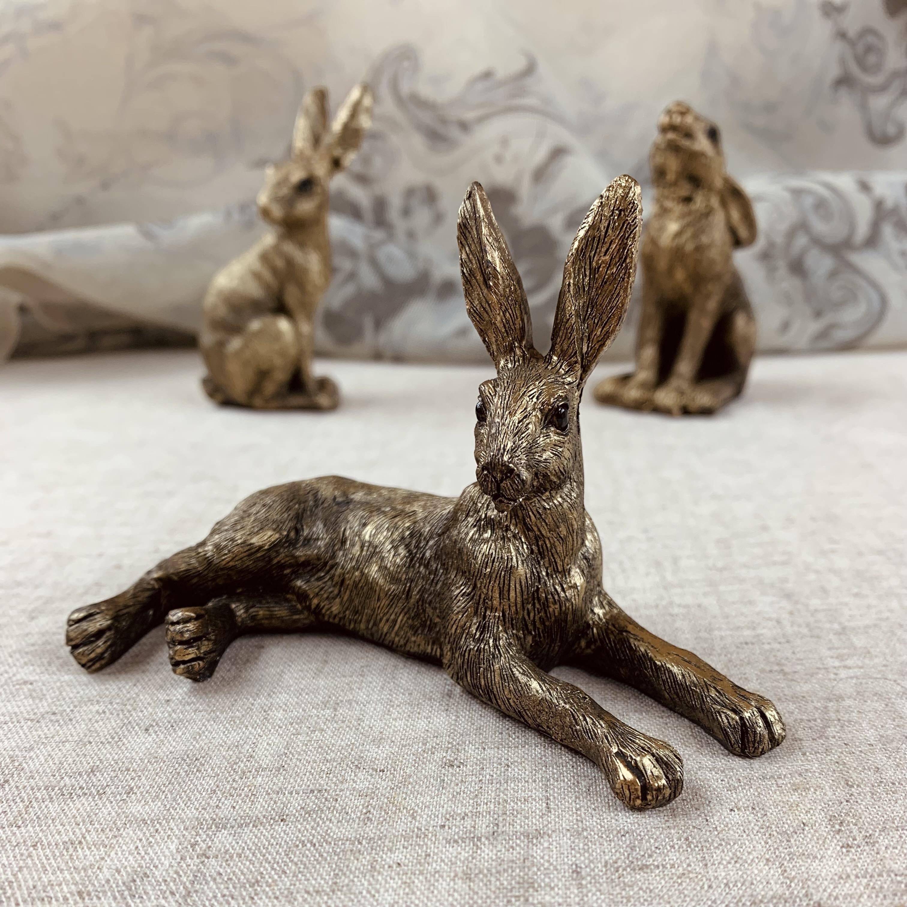 A set of three golden resin hares in different poses placed on a light-colored surface.