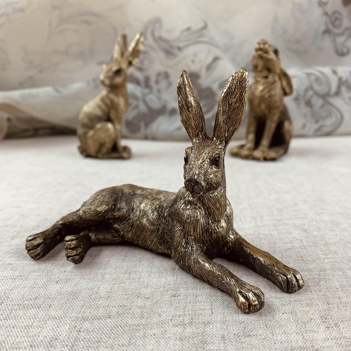 A set of three golden resin hares in different poses placed on a light-colored surface.