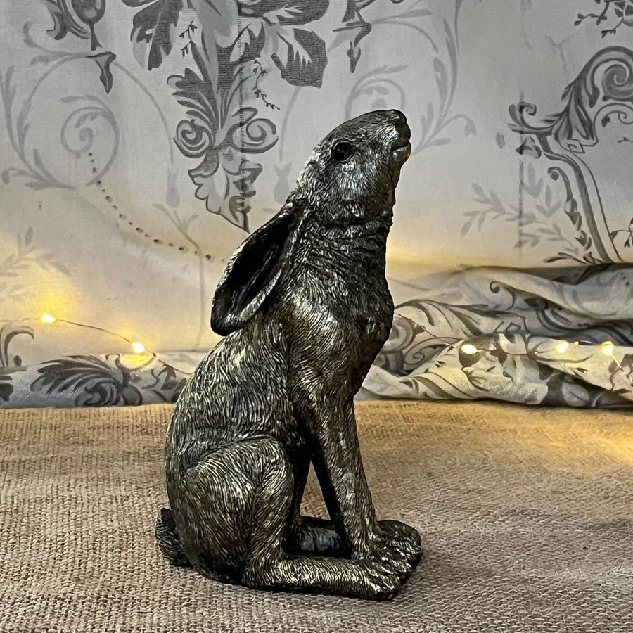 A bronze-colored resin ornament of a golden hare with an antique finish, sitting against a patterned background.