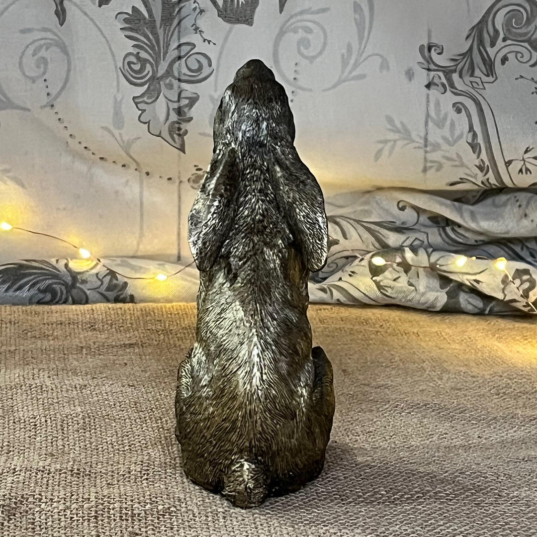 antique gold finish moon gazing hare facing away, showing it's back sat on textured surface with a soft focus fairy lights in the background