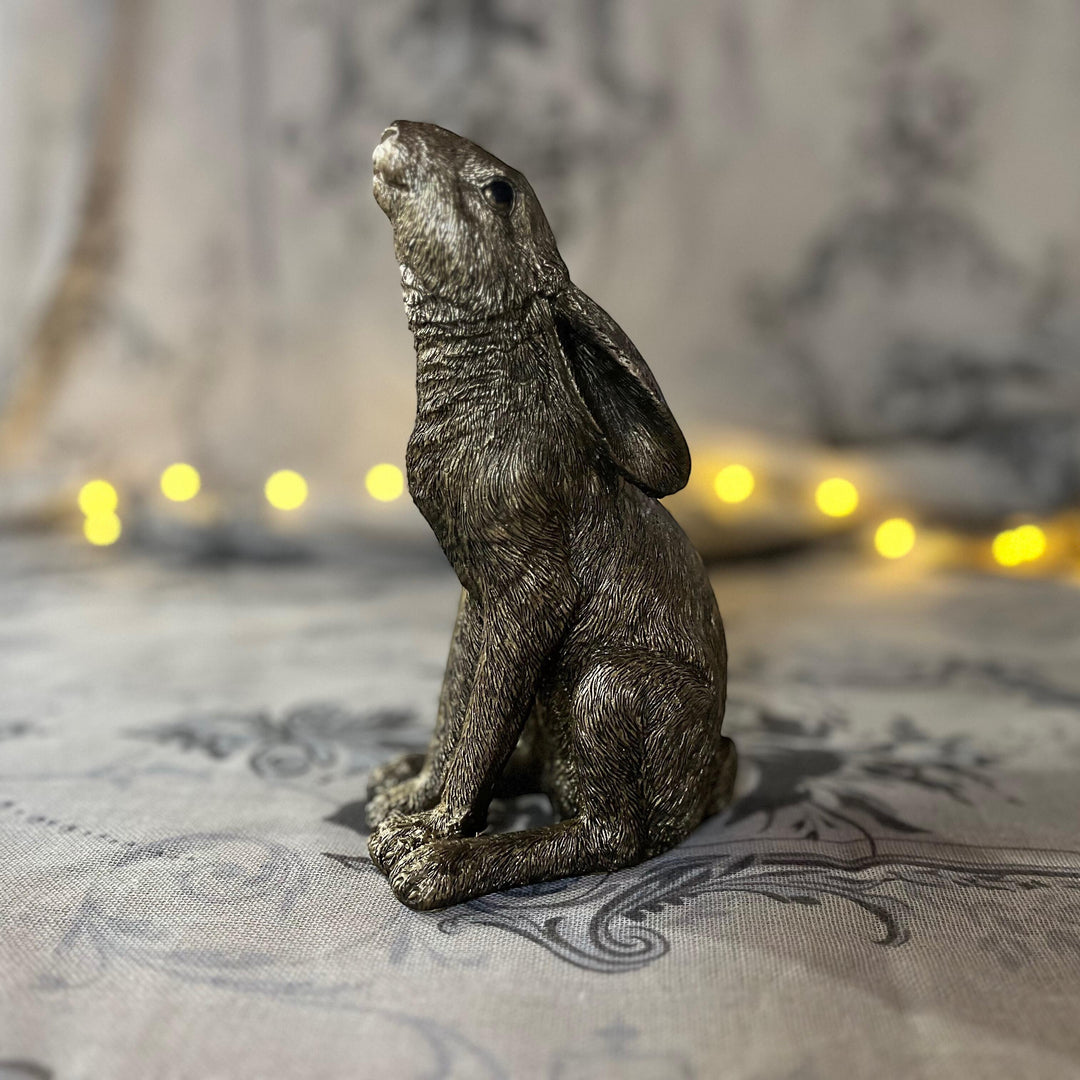 antique gold finish moon gazing hare sat on textured surface with a soft focus fairy lights in the background