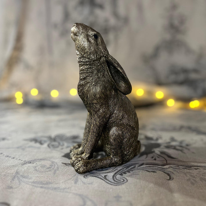 antique gold finish moon gazing hare sat on textured surface with a soft focus fairy lights in the background