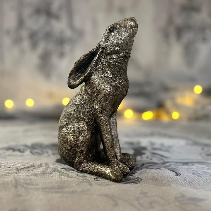 antique gold finish moon gazing hare sat on textured surface with a soft focus fairy lights in the background