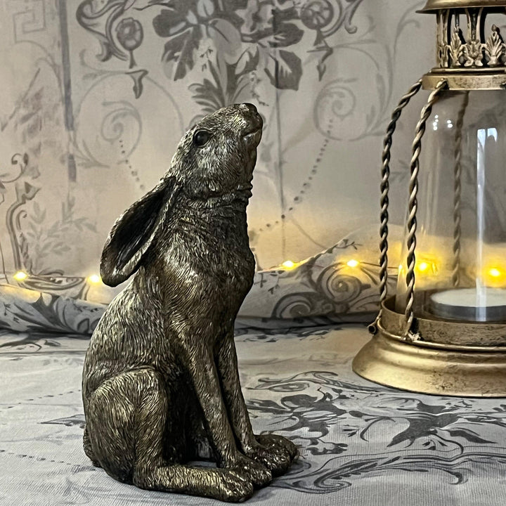 antique gold finish moon gazing hare sat on textured surface with a gold lantern behind