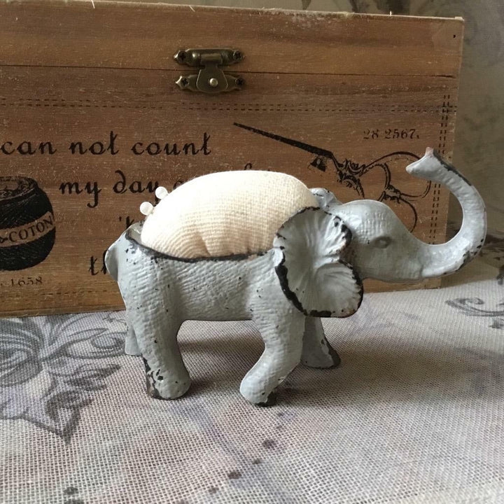 Shabby chic French grey metal elephant pin cushion with a padded hessian back and two sewing pins.