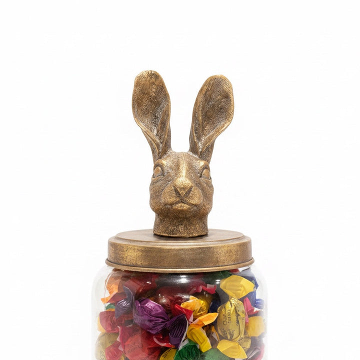 Large clear glass storage jar with a whimsical distressed golden hare lid filled with colourful confectionary