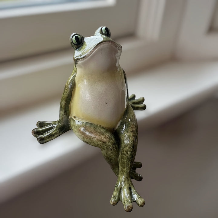 Green polyresin frog shelf sitter with crossed legs and hand-finished vintage style details, sittting on a window ledge