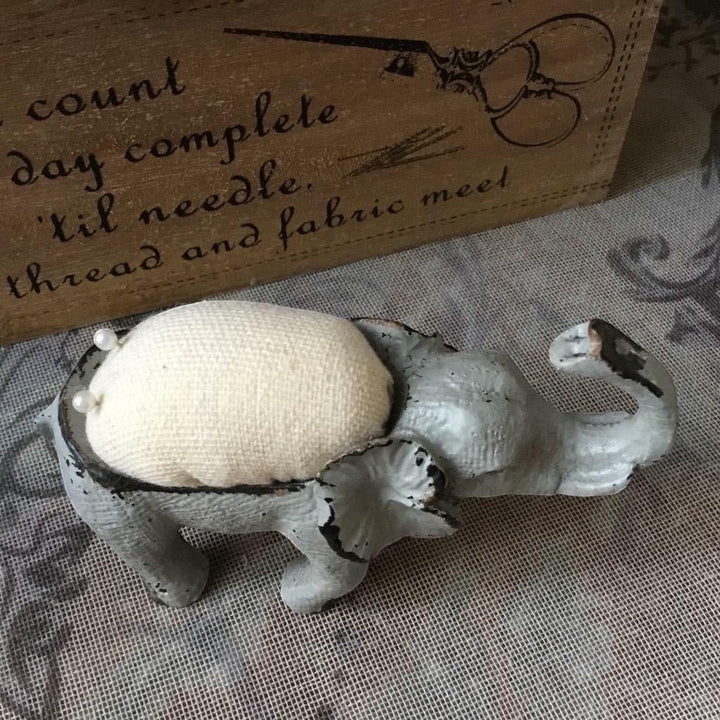 Shabby chic elephant pin cushion in French grey metal with a cream hessian padded back and two pins.