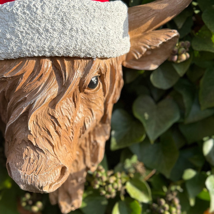 Resin cow head with a Santa hat against a green leafy background