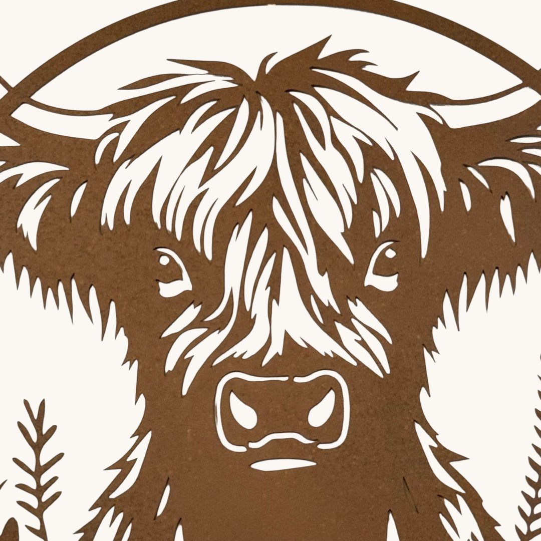 A close-up of a brown laser-cut metal wall art piece featuring the face of a shaggy Highland cow, shown against a white background.