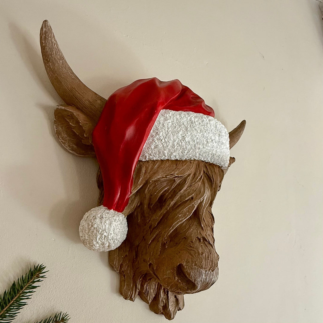 Resin Highland cow wall hanger wearing a festive red and white Santa hat for Christmas home decor.
