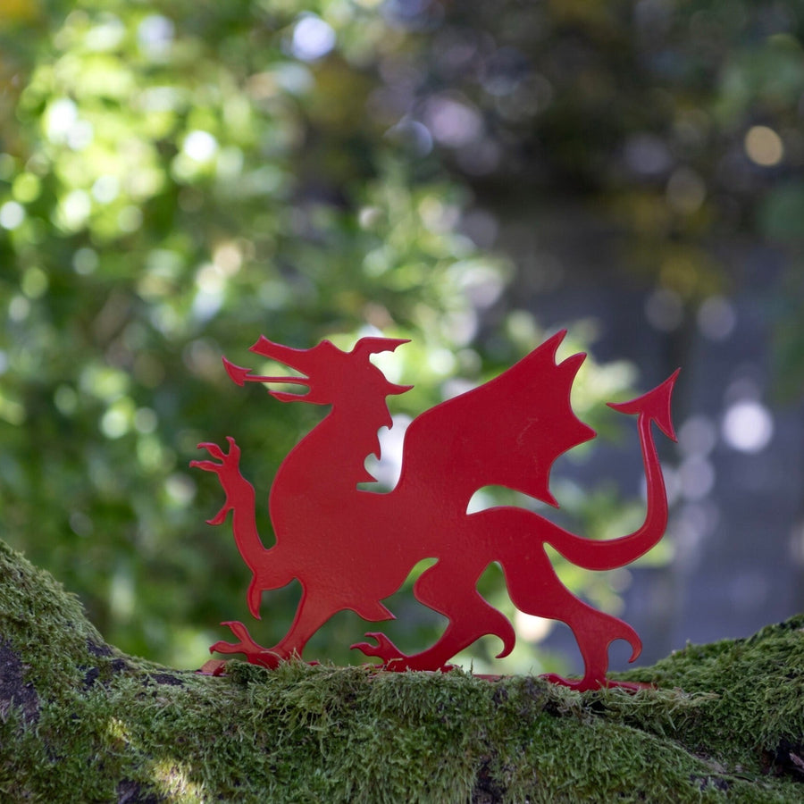 A bright red metal dragon decoration placed on a green mossy surface with trees in the background.