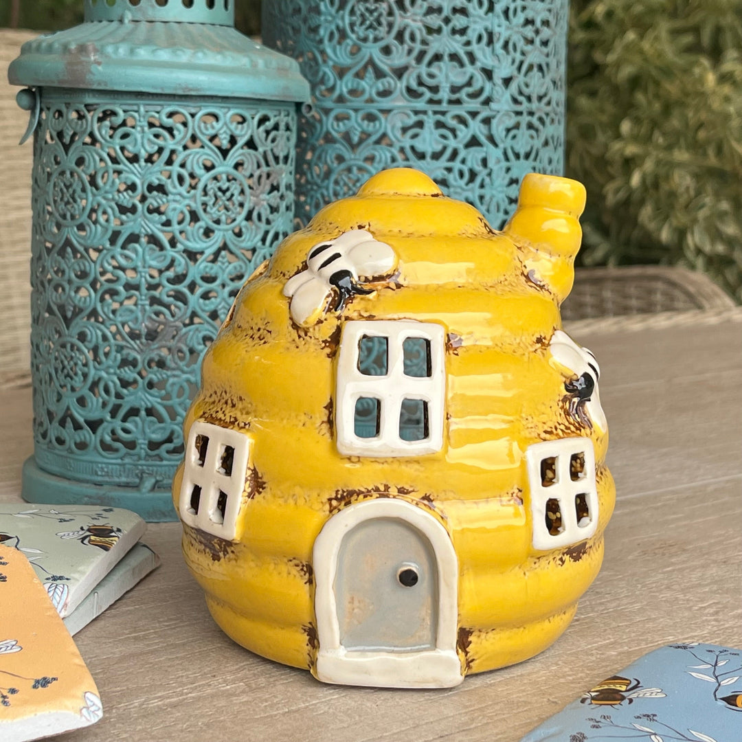 Yellow ceramic beehive with bees on a wooden surface with blue lanterns in the background