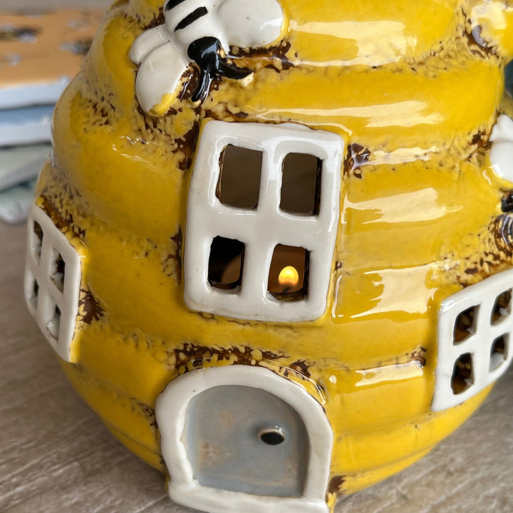 Yellow ceramic beehive with a small candle inside on a wooden surface