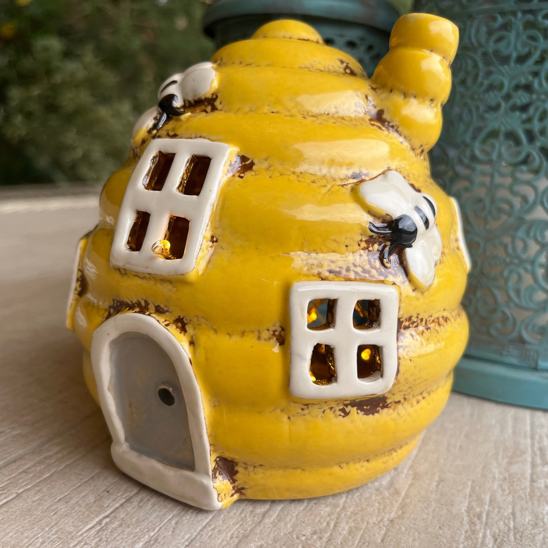 Yellow ceramic house-shaped lantern with decorative elements on a wooden surface.