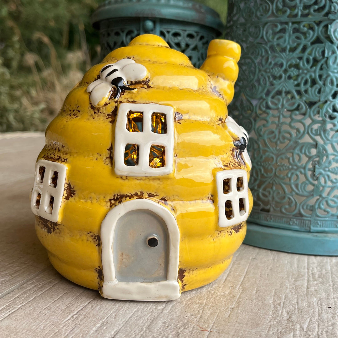 Yellow ceramic beehive-shaped object with small windows and a door on a wooden surface.